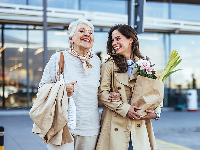 Two women smiling after shopping, holding flowers together.
