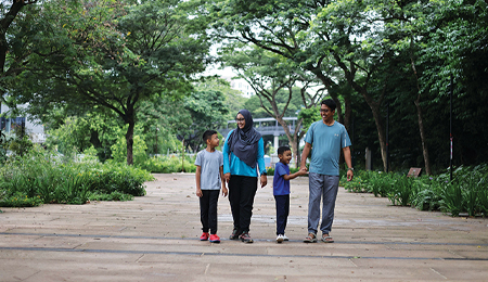 Muslim family of 4 walking on park broadwalk surrounded by greenery